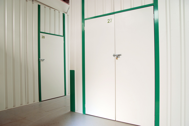 Two storage unit doors labeled 27 and 28 with green frames and padlocks. These business storage solutions are situated in a clean, well-lit facility.