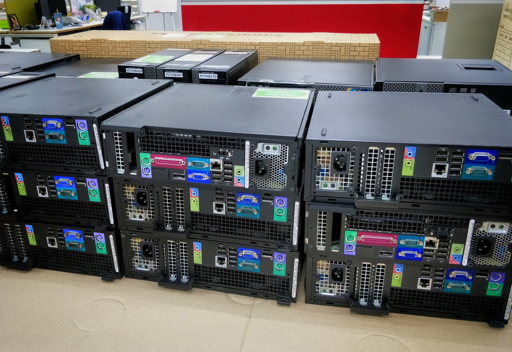 Several black computer towers are stacked in two rows on a desk in an office setting, with various colored ports visible on their back panels, ready for efficient office moves.