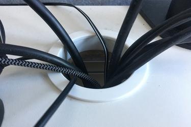 Several black cables pass through a white circular cable management grommet on a desk.