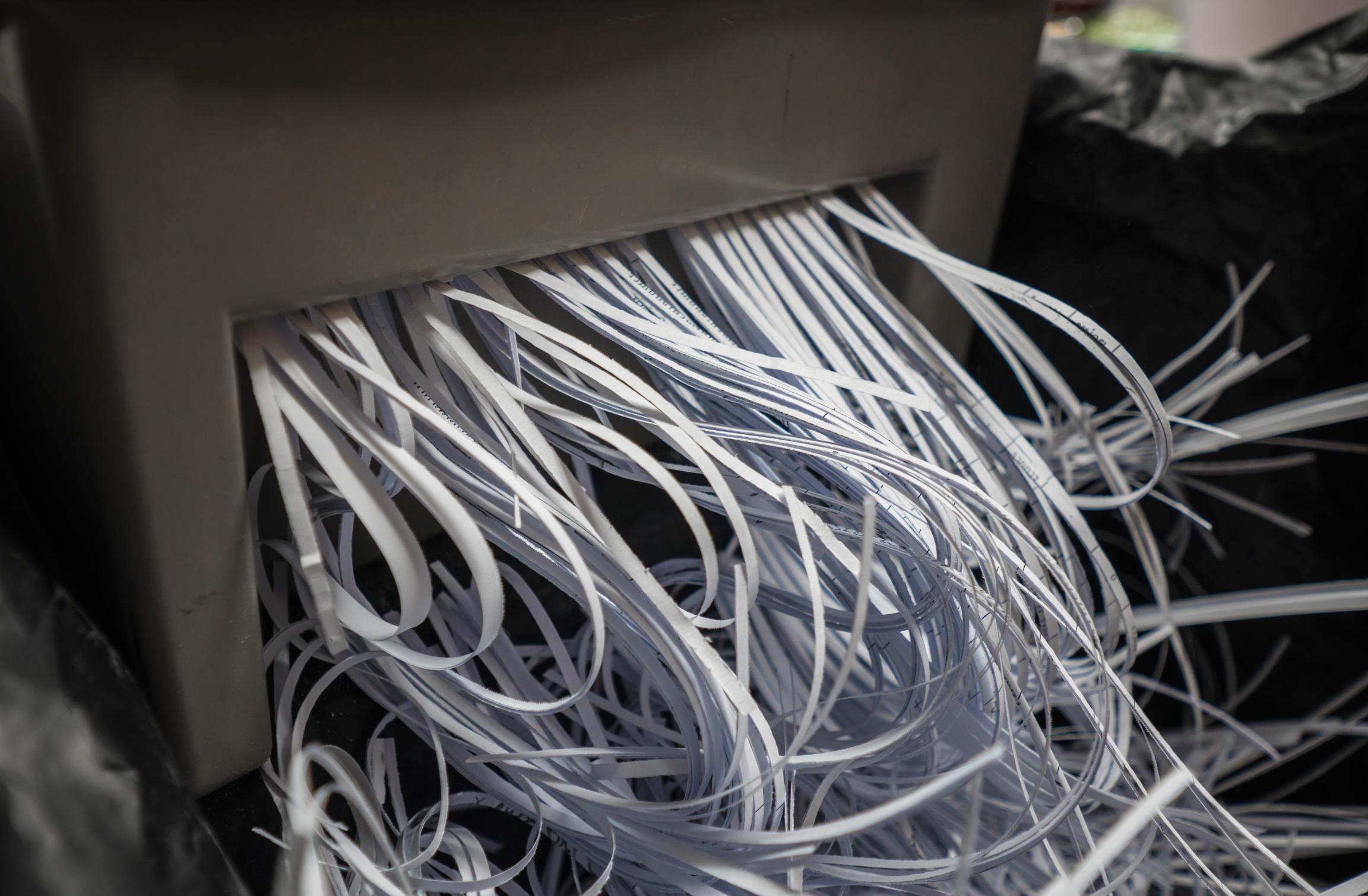 Close-up of a paper shredder with strips of shredded paper being ejected from the machine.